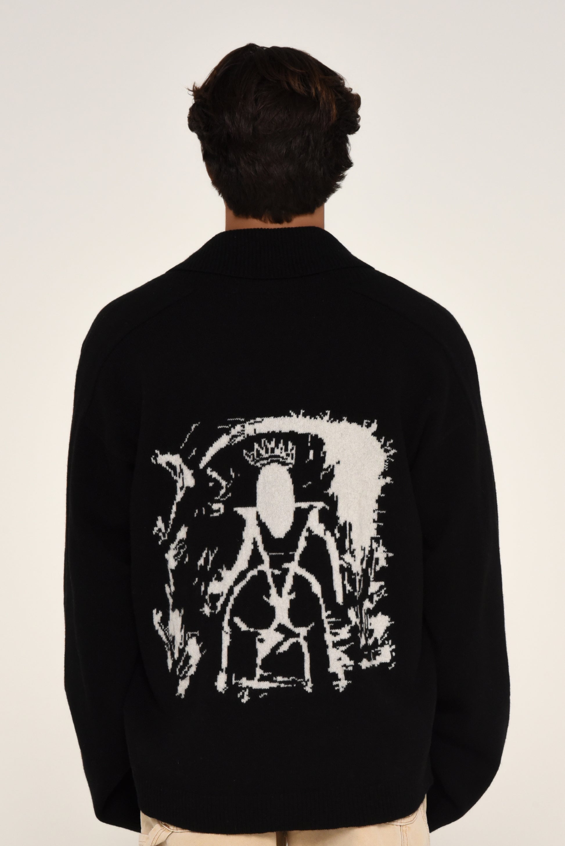 Man wearing a black cardigan with a white graphic design of a woman on the back 
