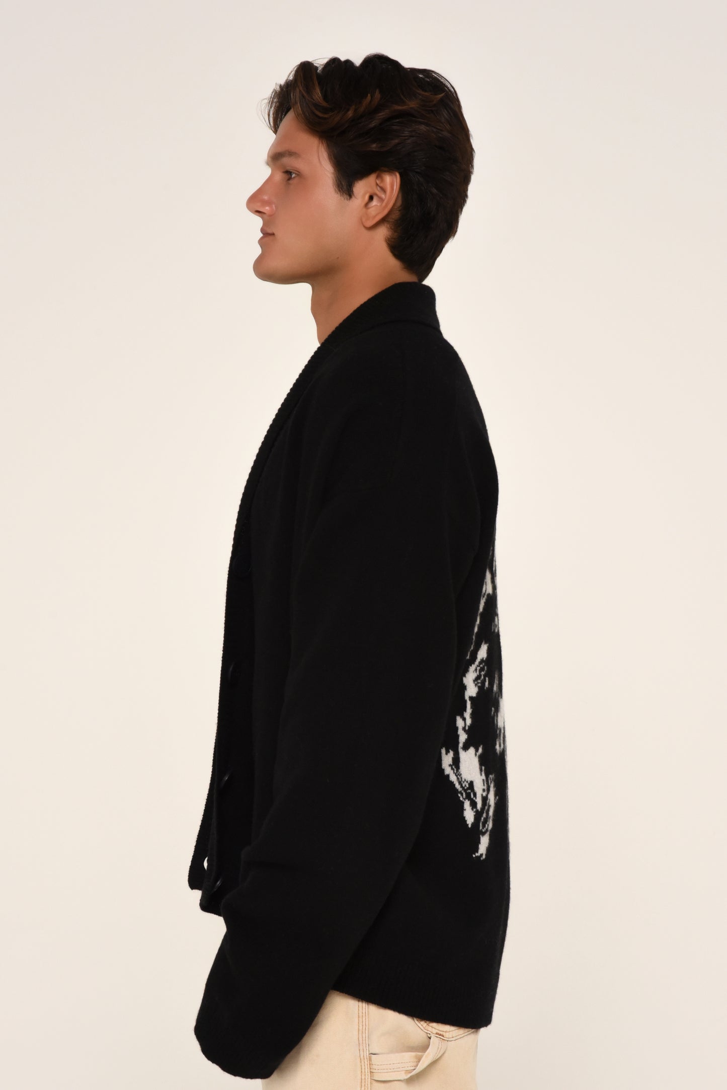 Side view of man wearing a black cardigan with a white graphic design of a woman on the back 