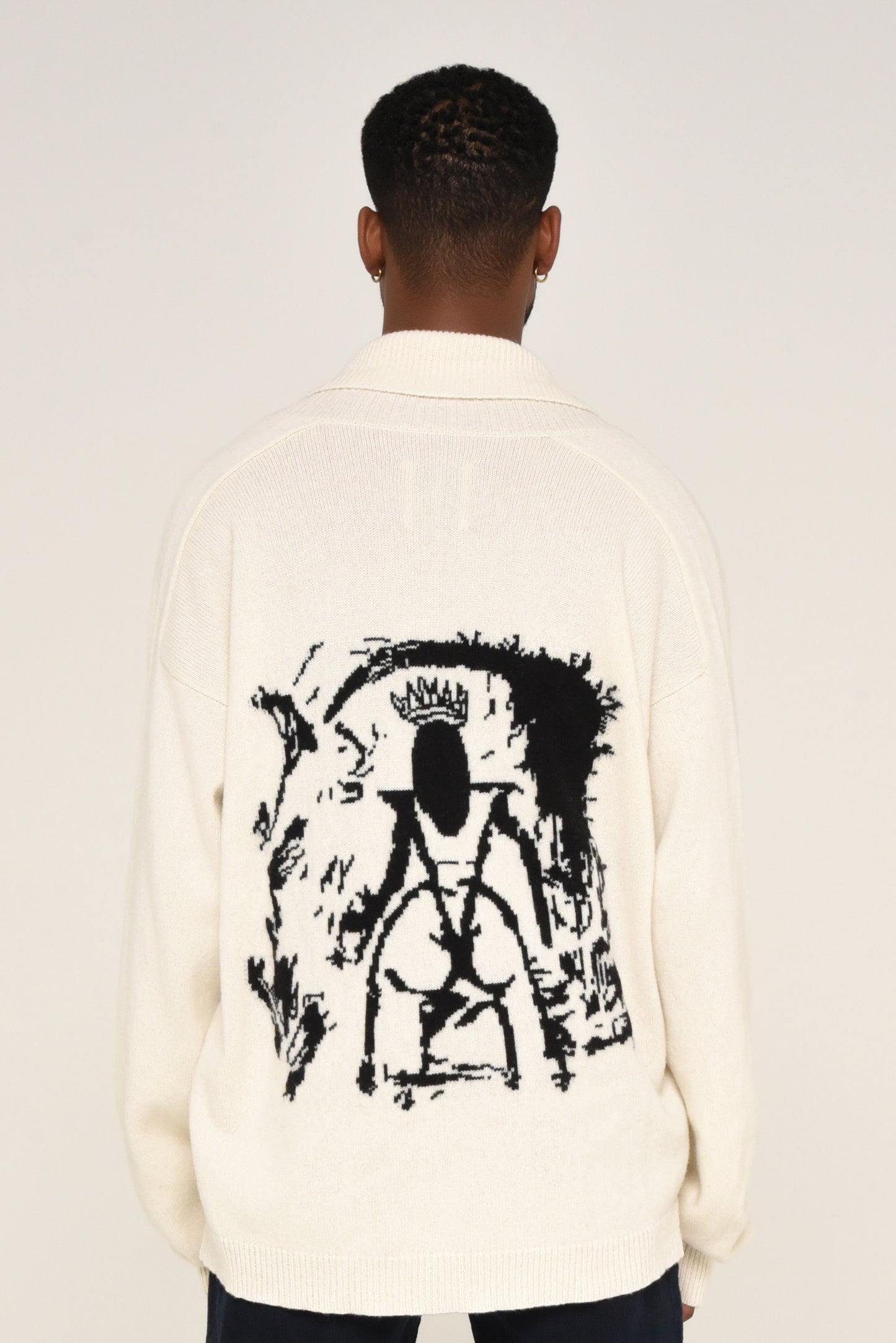 Back view of man wearing a white cardigan with a black graphic design of a woman on the back 