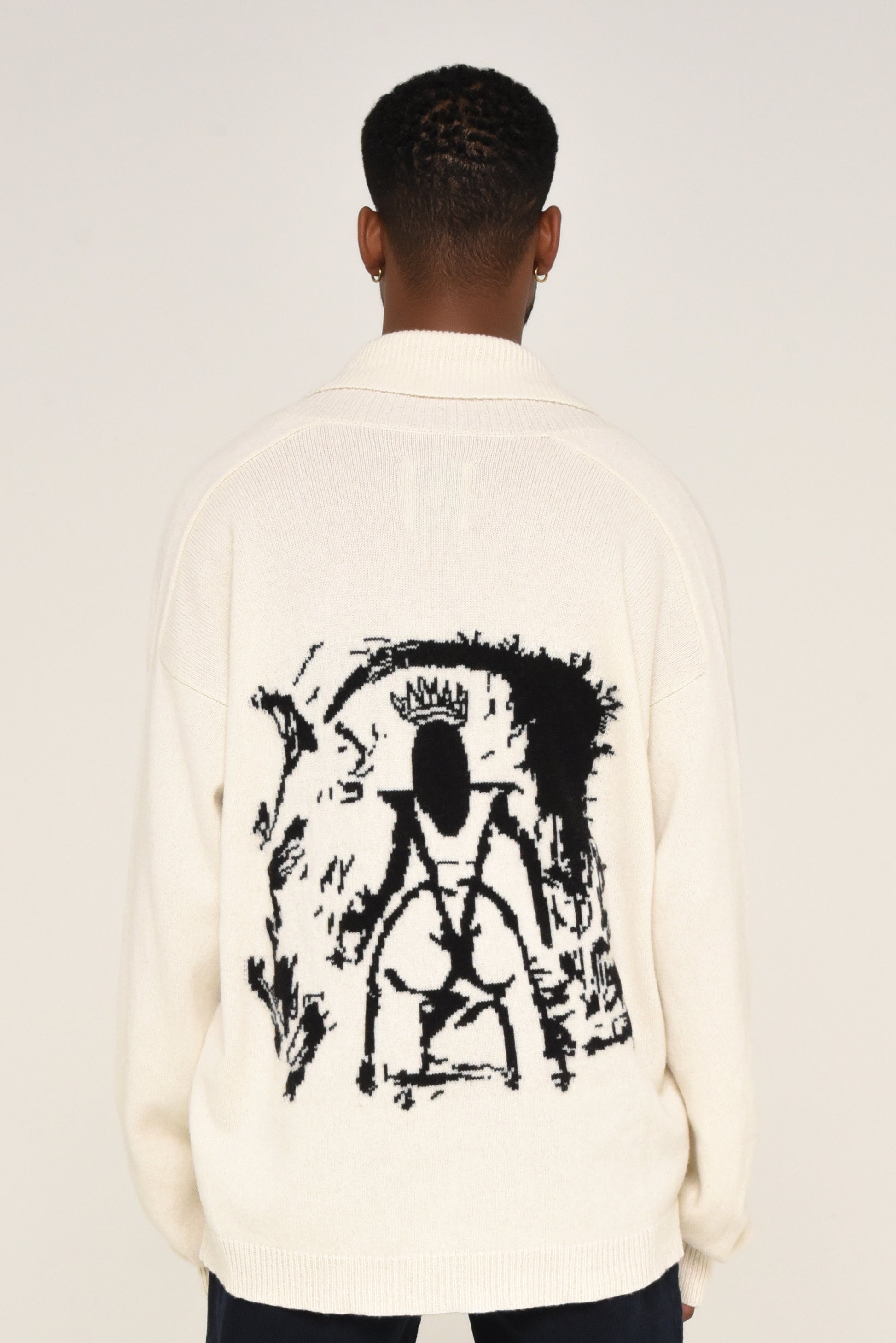 Back view of man wearing a white cardigan with a black graphic design of a woman on the back 