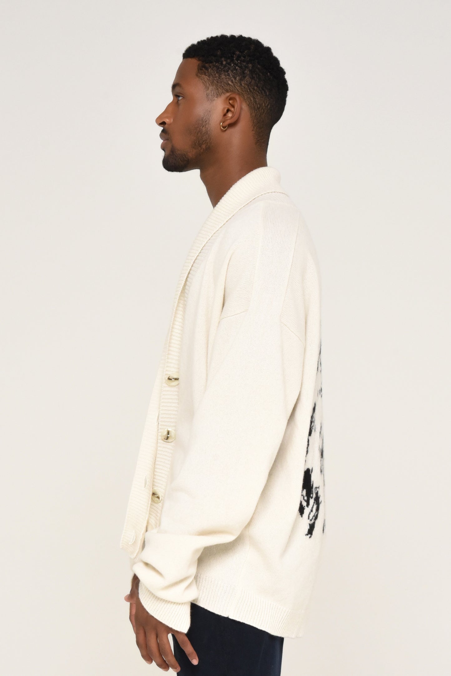Side view of man wearing a white cardigan with a black graphic design of a woman on the back 