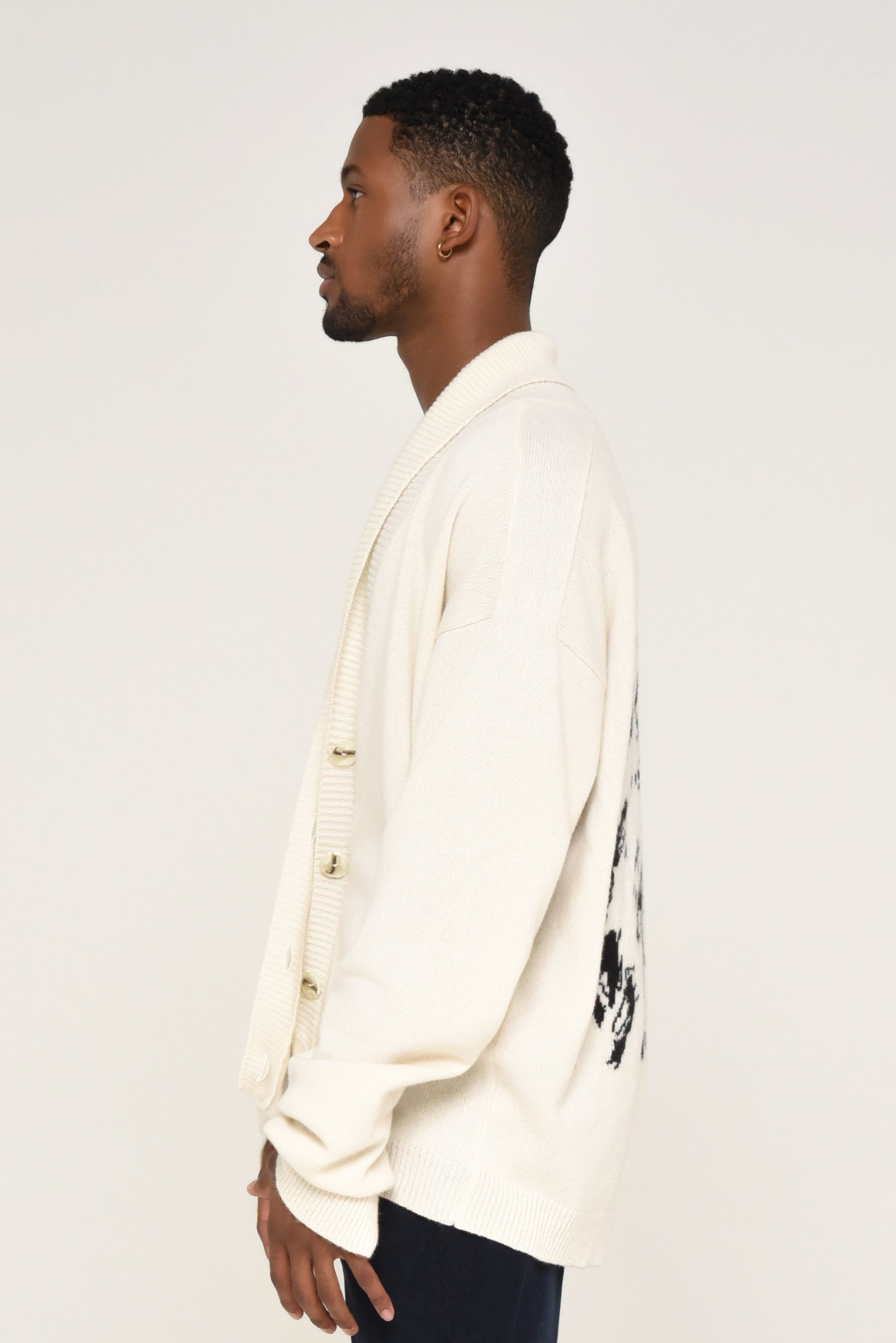 Side view of man wearing a white cardigan with a black graphic design of a woman on the back 