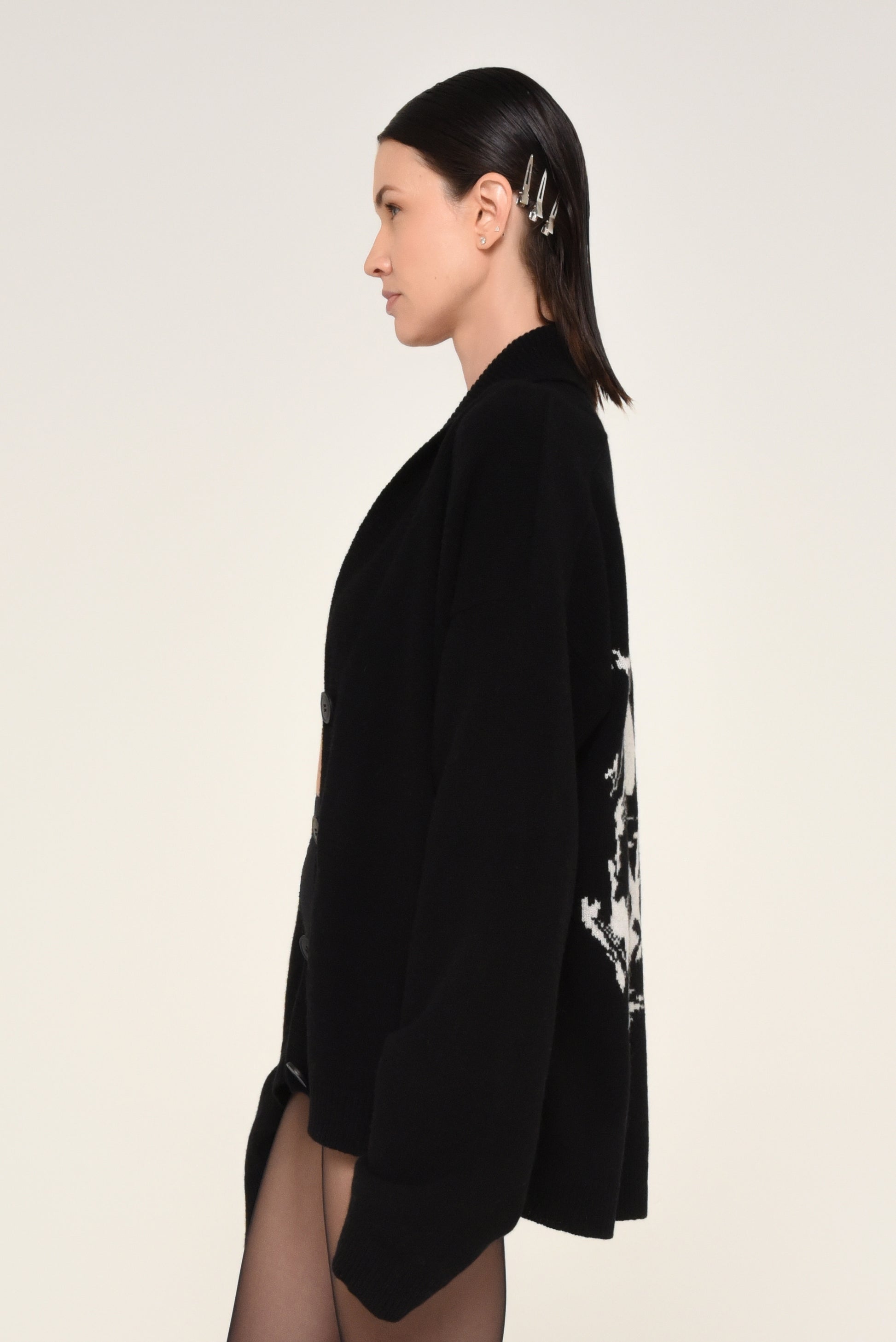 Side view of woman wearing a black cardigan with a white graphic design of a woman on the back 