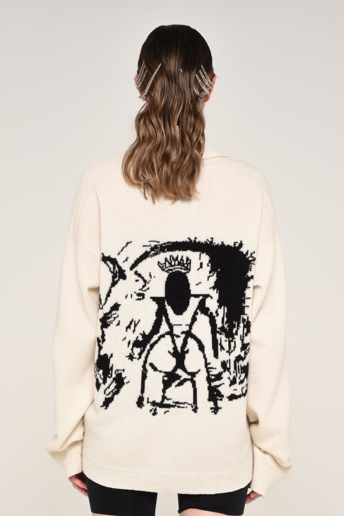 Back view of woman wearing a cream cardigan with a black graphic design of a woman on the back 