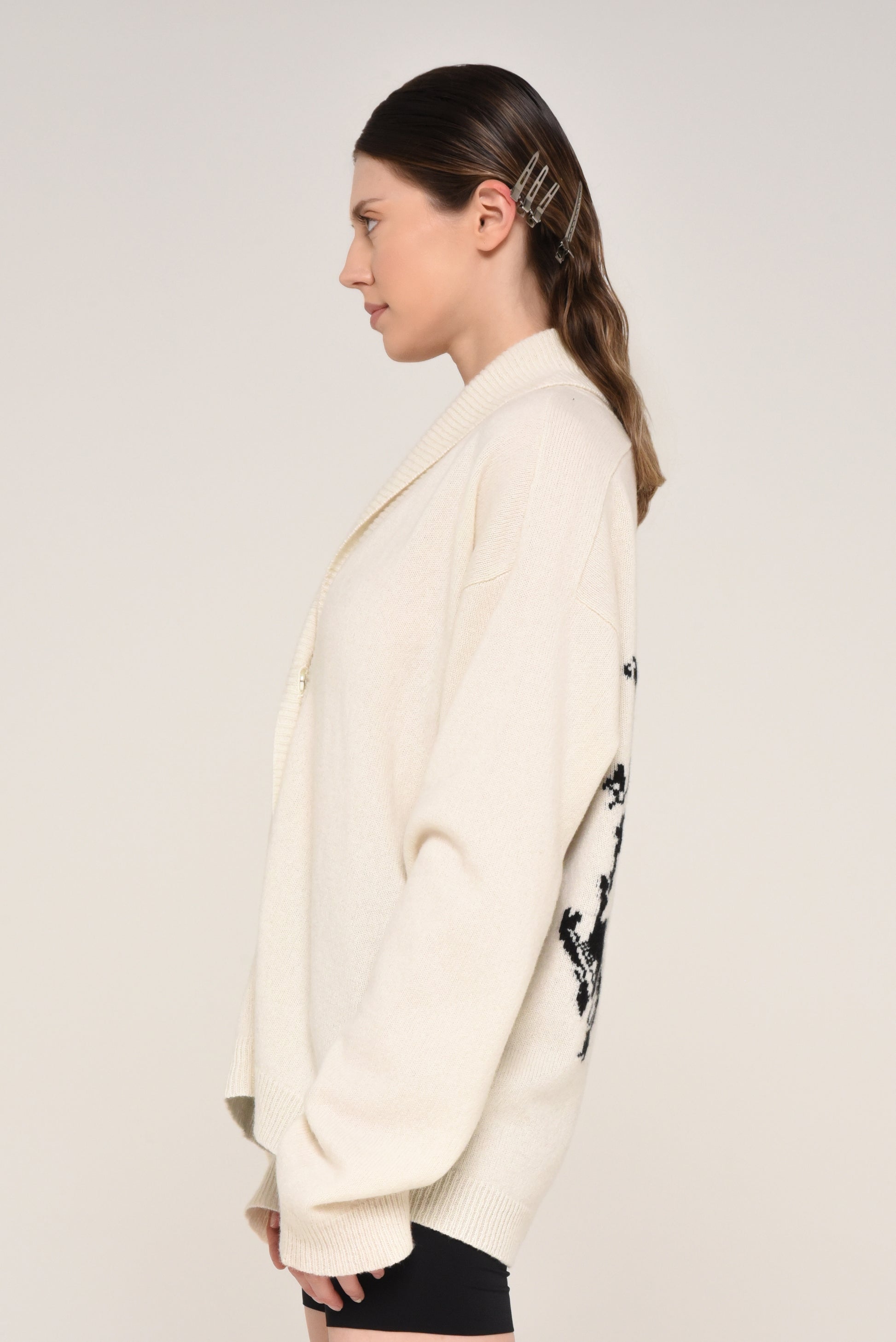 Side view of woman wearing a cream cardigan with a black graphic design of a woman on the back 