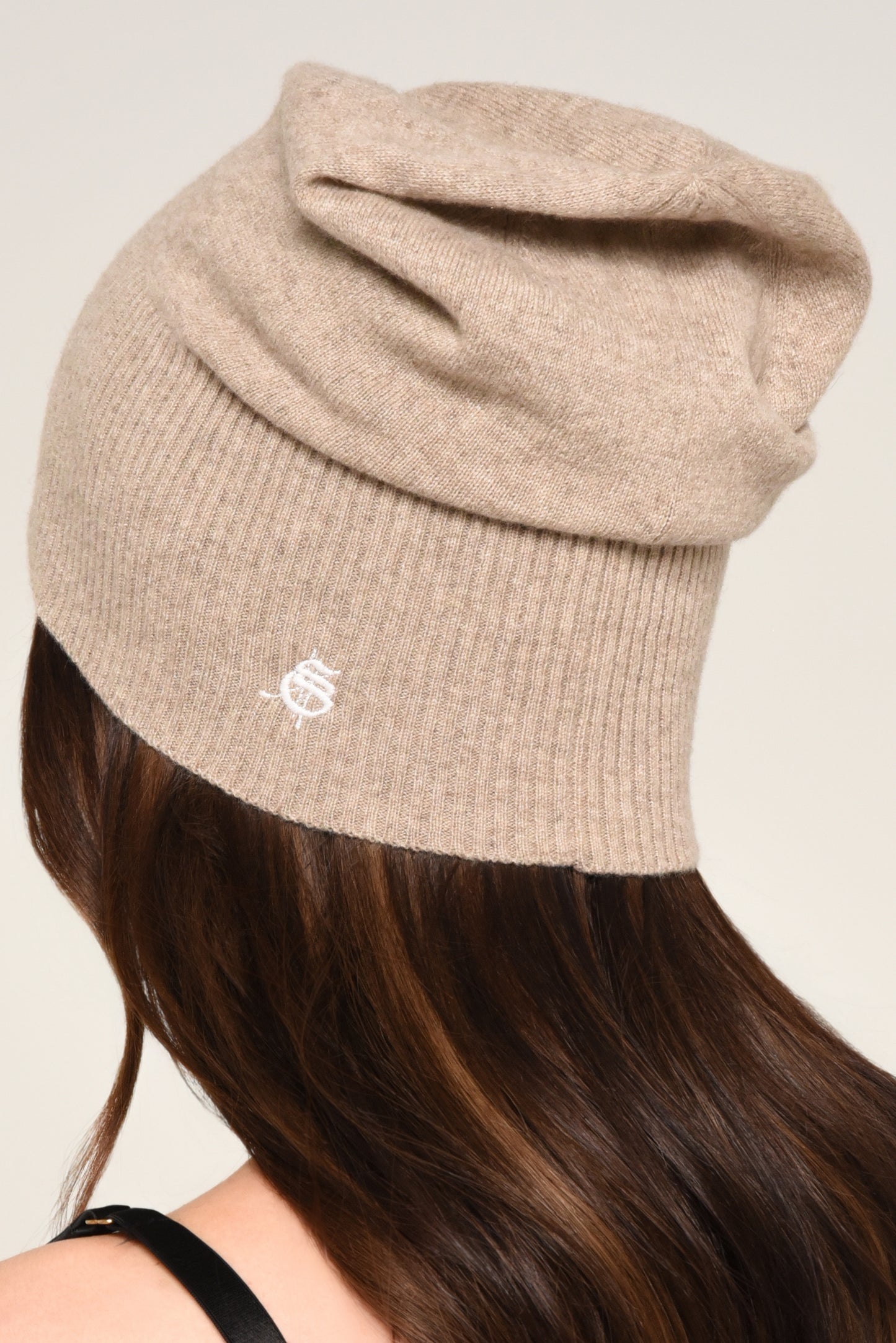 back view of woman wearing a slouchy beige knit beanie with embroidery 