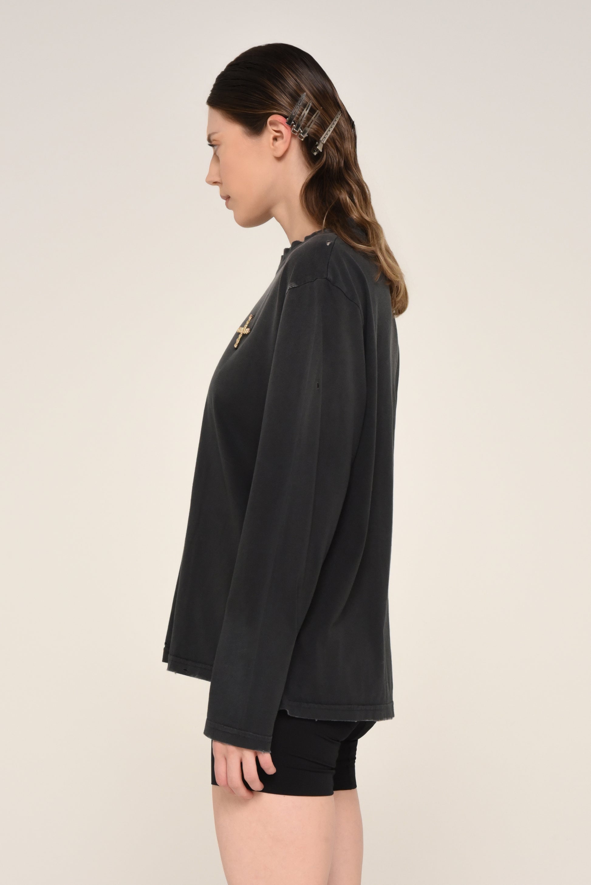 Side view of woman wearing a black long sleeve shirt with embroidered cross logo and biker shorts