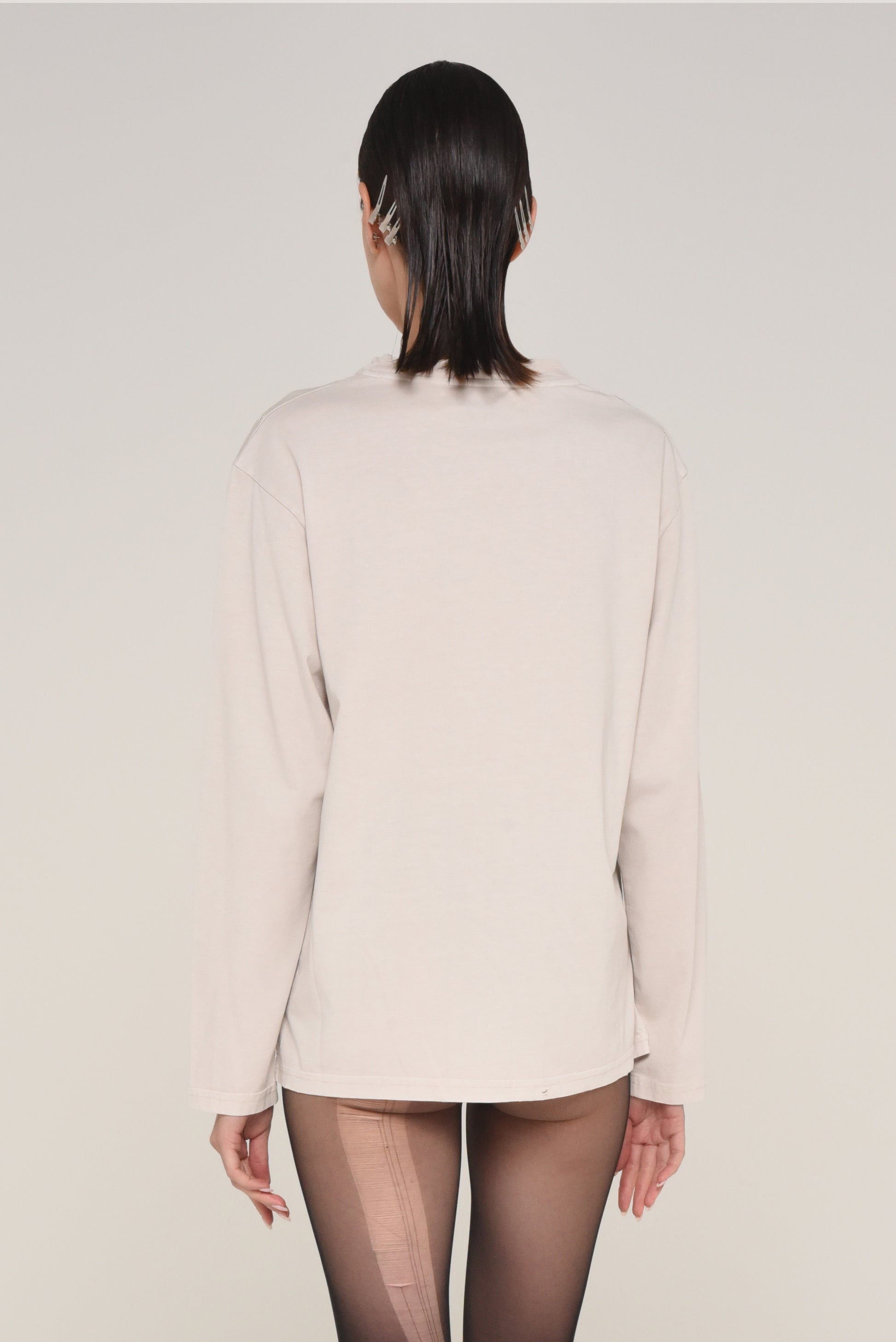 back view of woman wearing an off-white long sleeve shirt and ripped tights