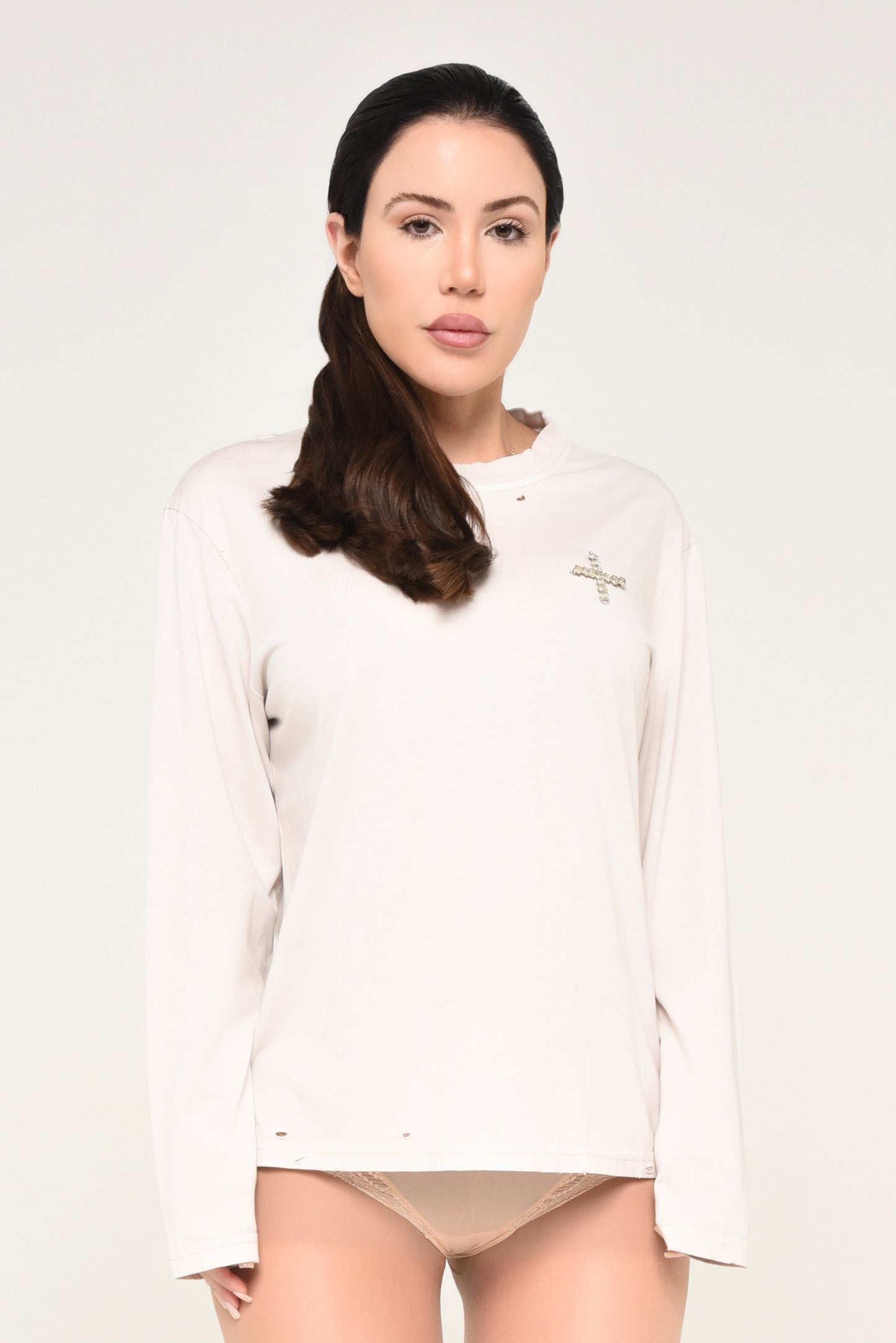 Woman wearing an off-white long sleeve shirt with embroidered cross detail, styled as a neutral streetwear look.