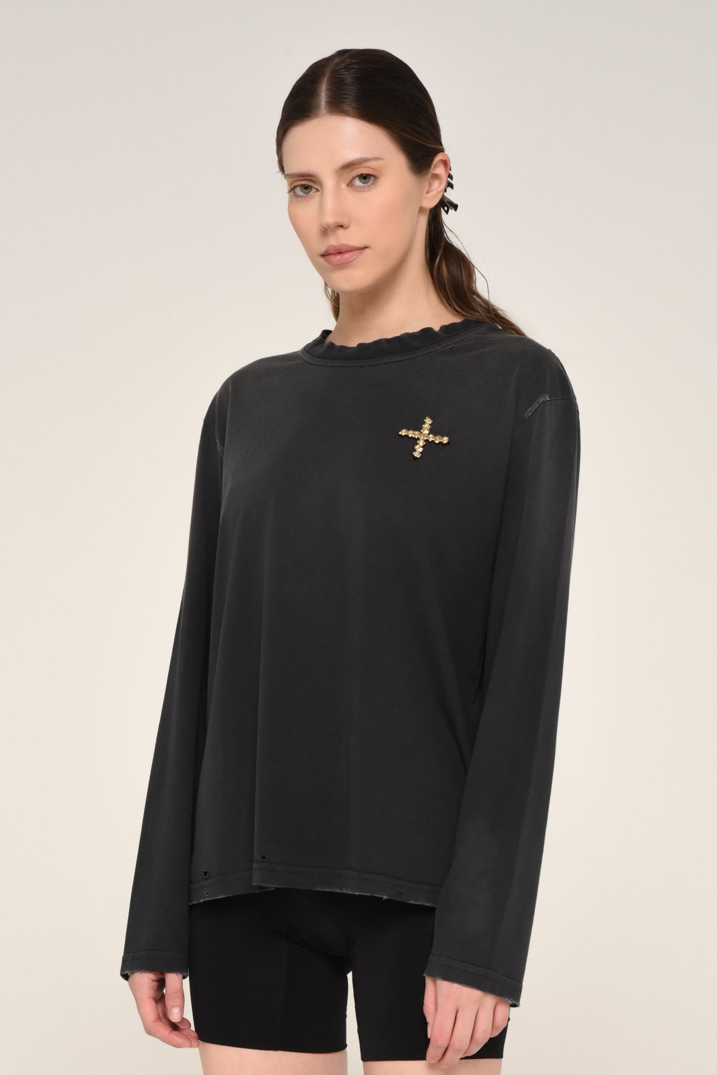 Woman wearing a black long sleeve shirt with embroidered cross logo and biker shorts