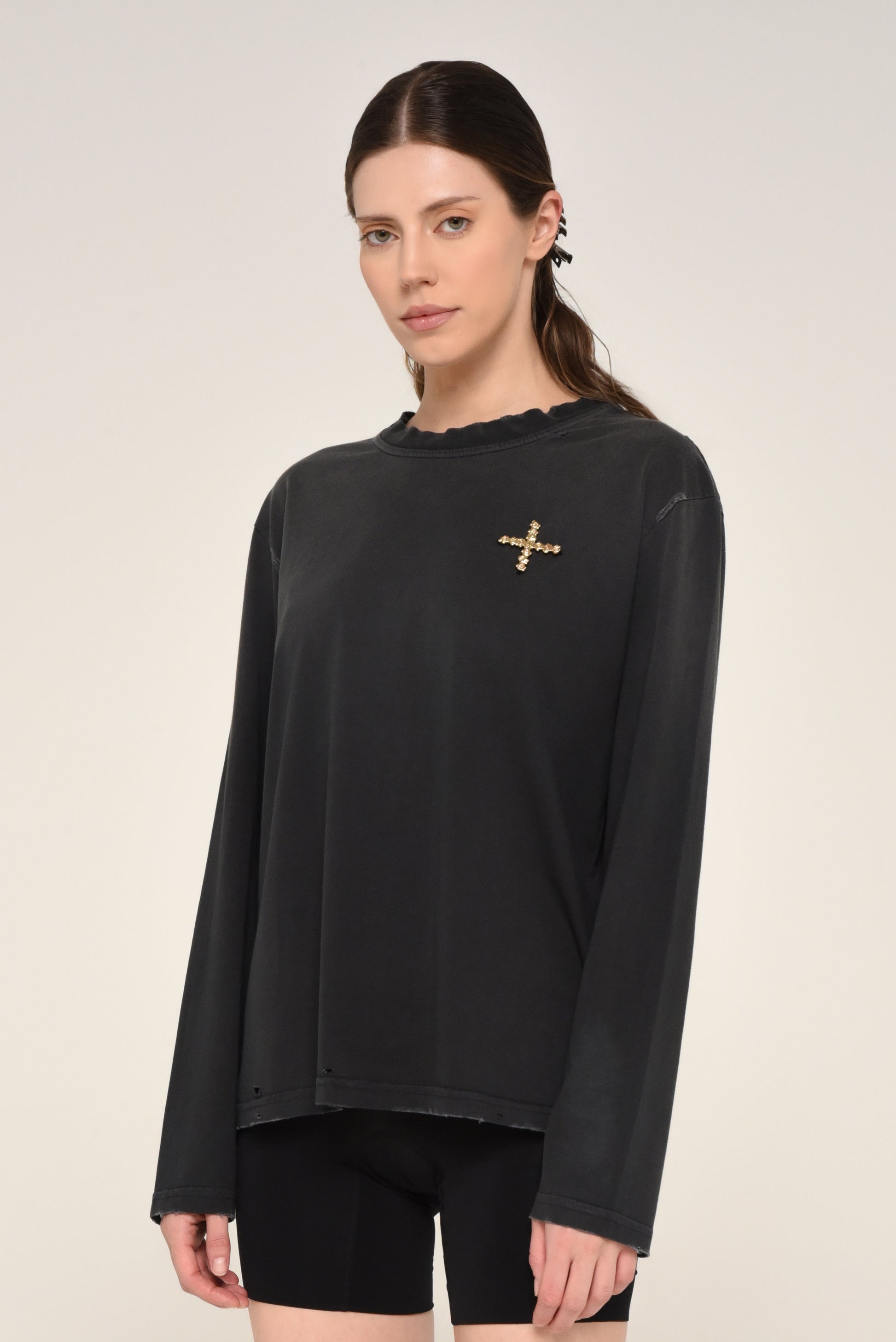 Woman wearing a black long sleeve shirt with embroidered cross logo and biker shorts