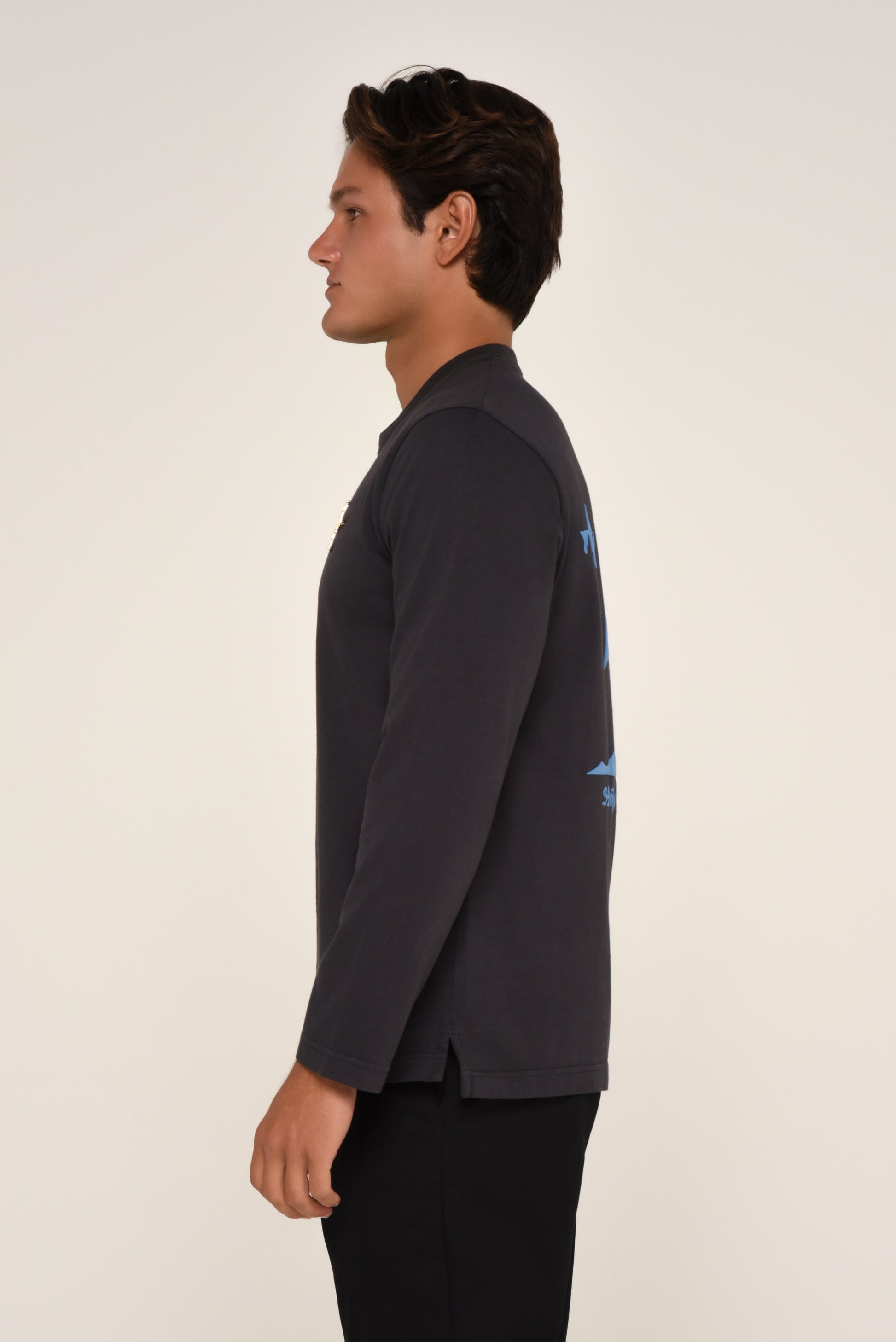 Side view of man wearing a black long-sleeve shirt with cross detail and red text