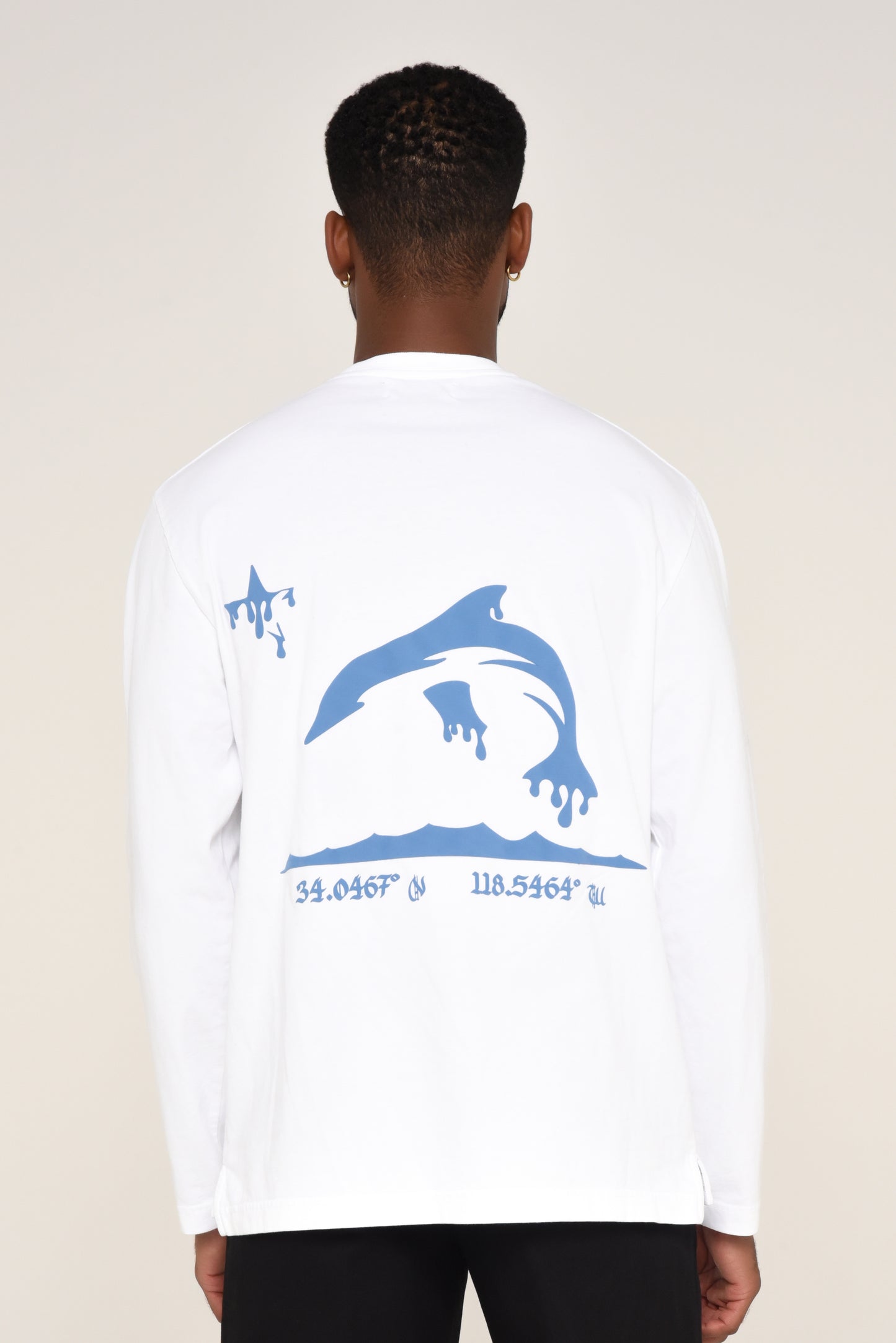 White long-sleeve shirt with blue dolphin graphic and coordinates on a beige background. 