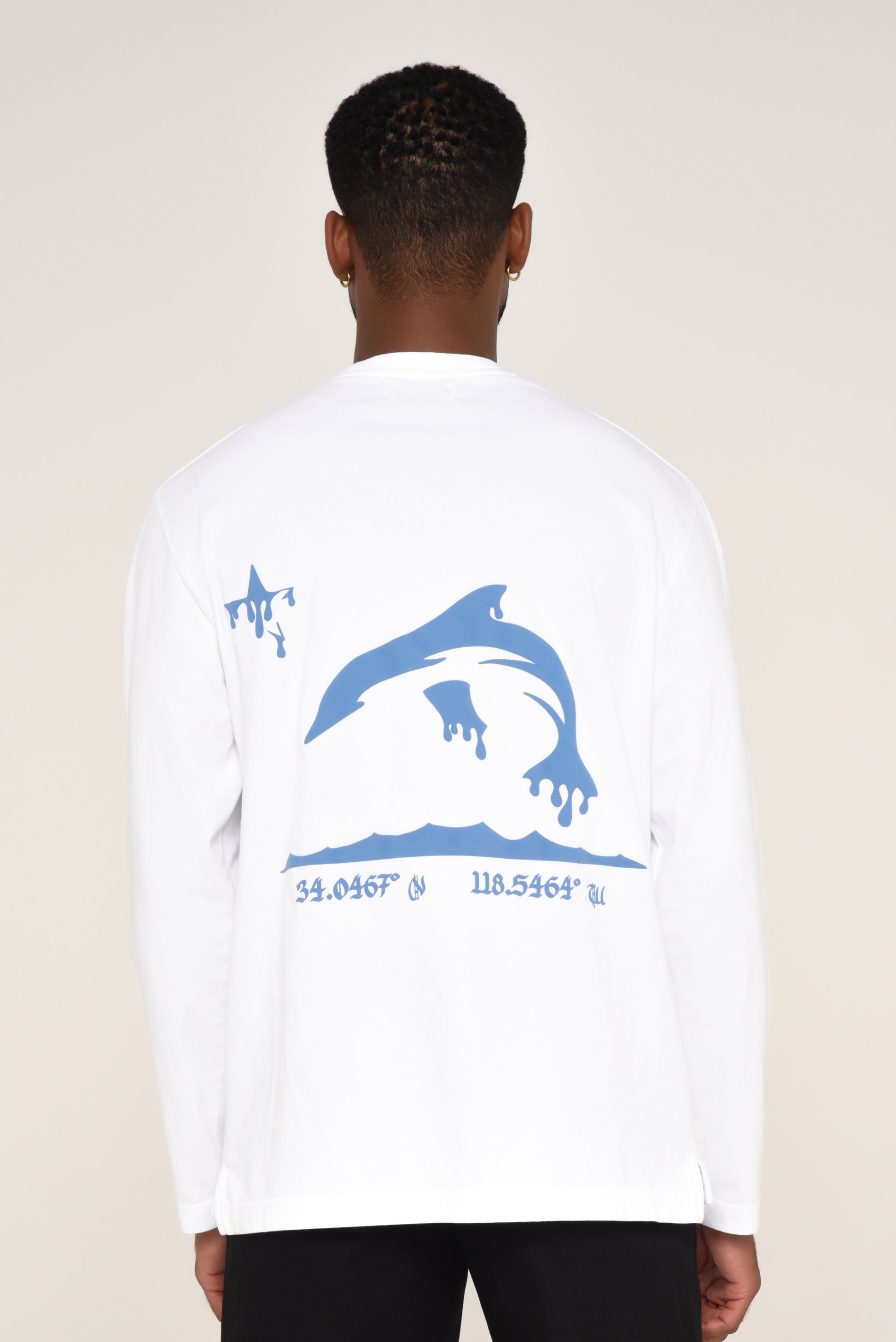 White long-sleeve shirt with blue dolphin graphic and coordinates on a beige background. 