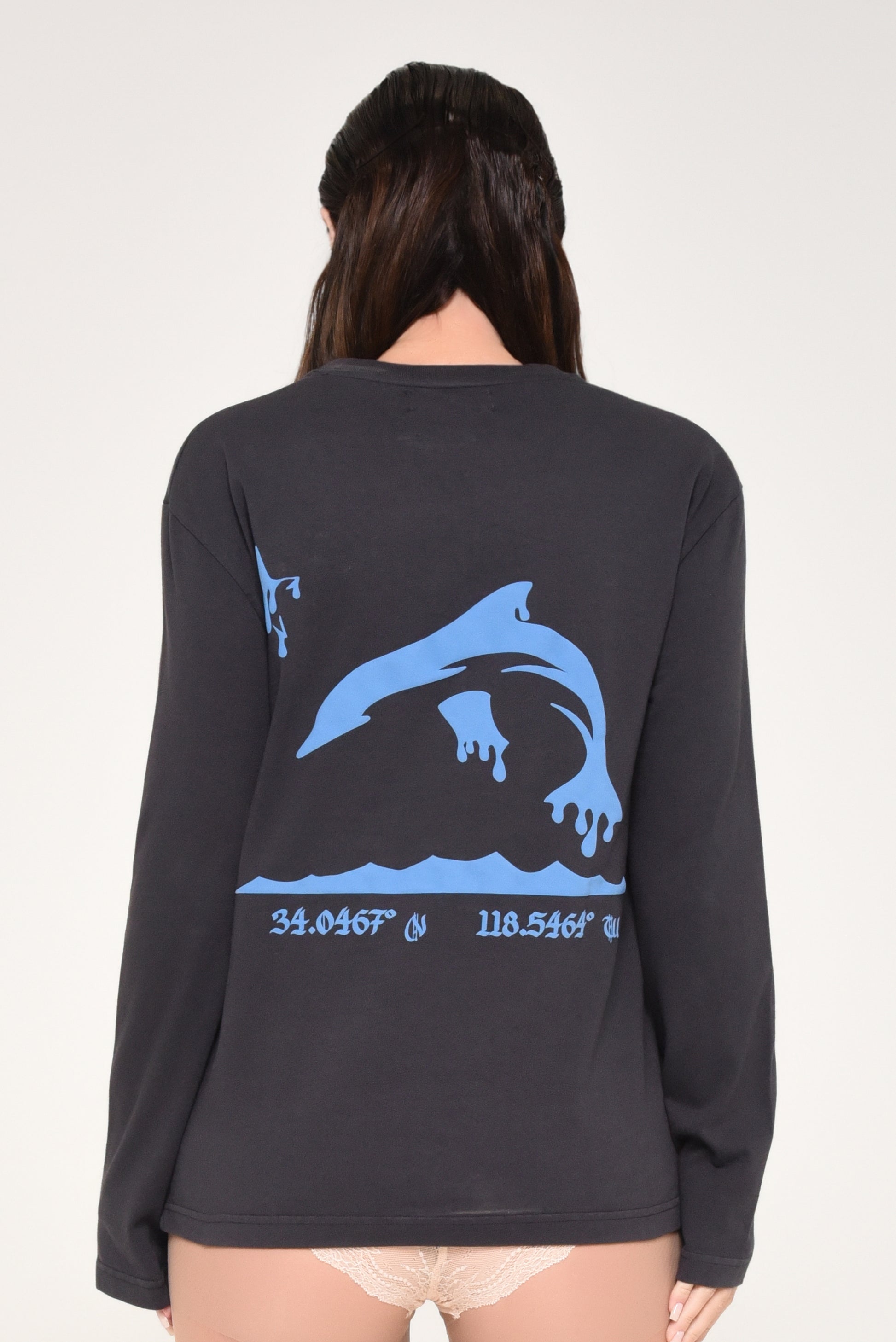 Black long-sleeve shirt with blue dolphin graphic and coordinates on a beige background