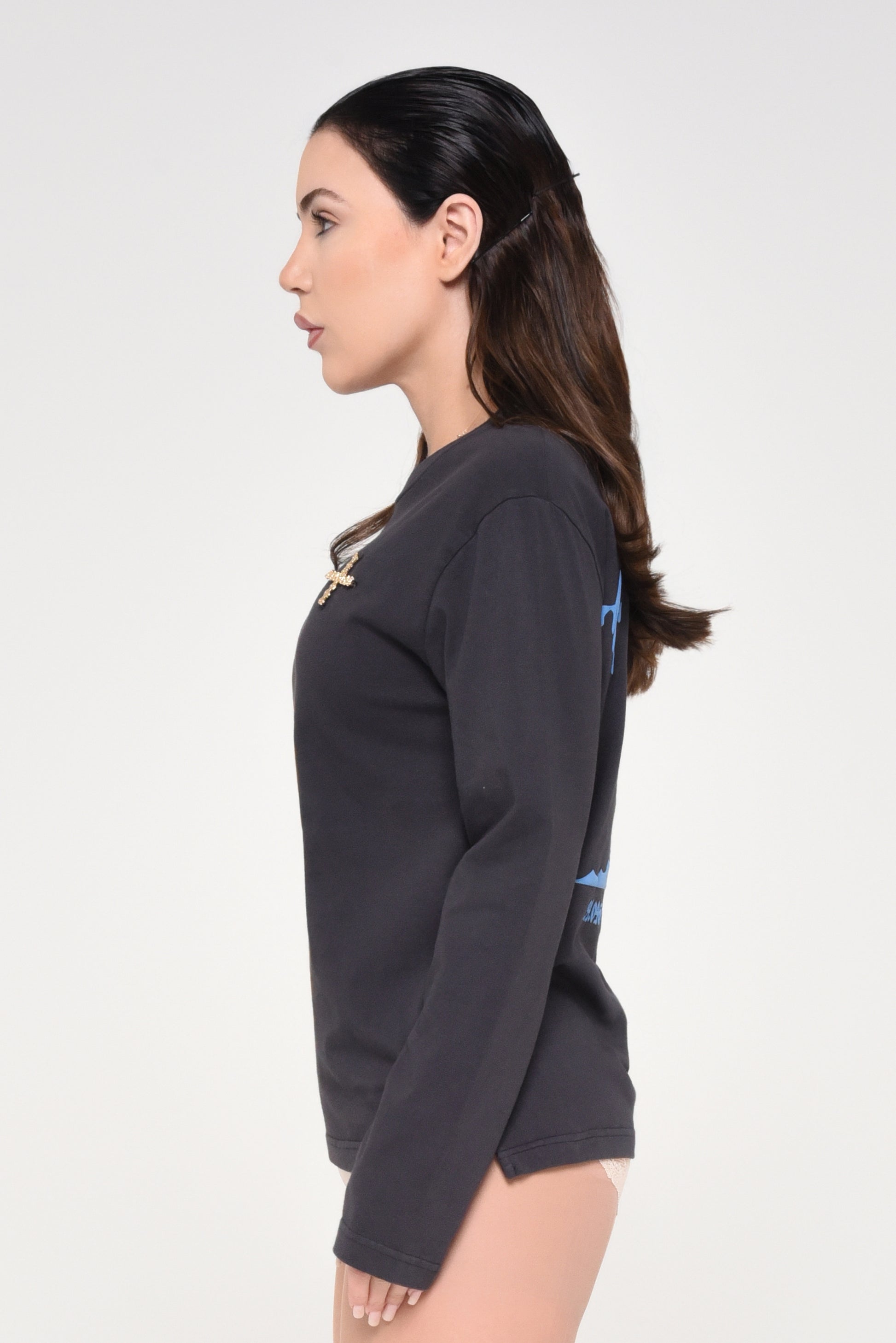 Side view of woman wearing a black long-sleeve shirt with cross detail and red text