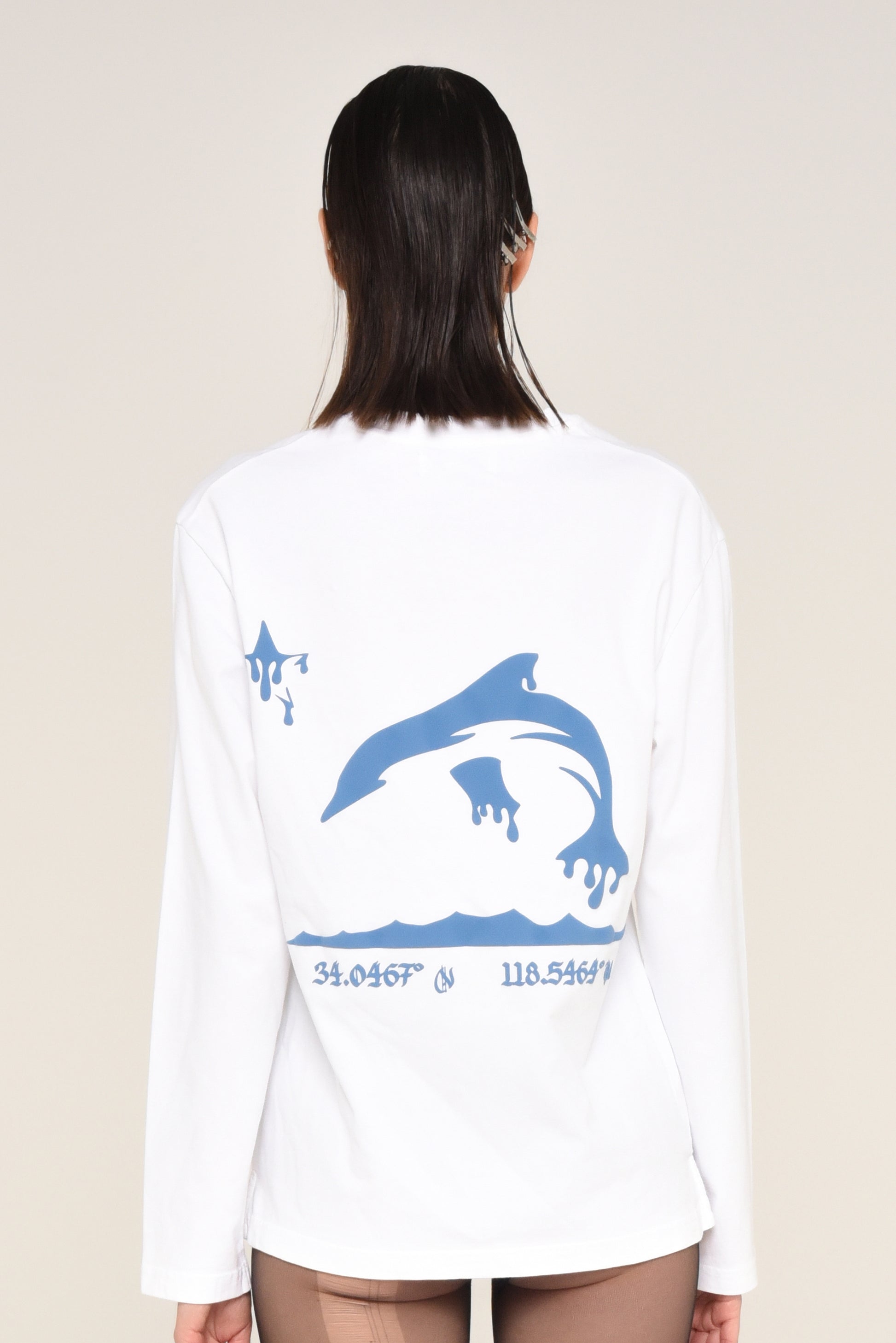 White long-sleeve shirt with blue dolphin graphic and coordinates on a beige background