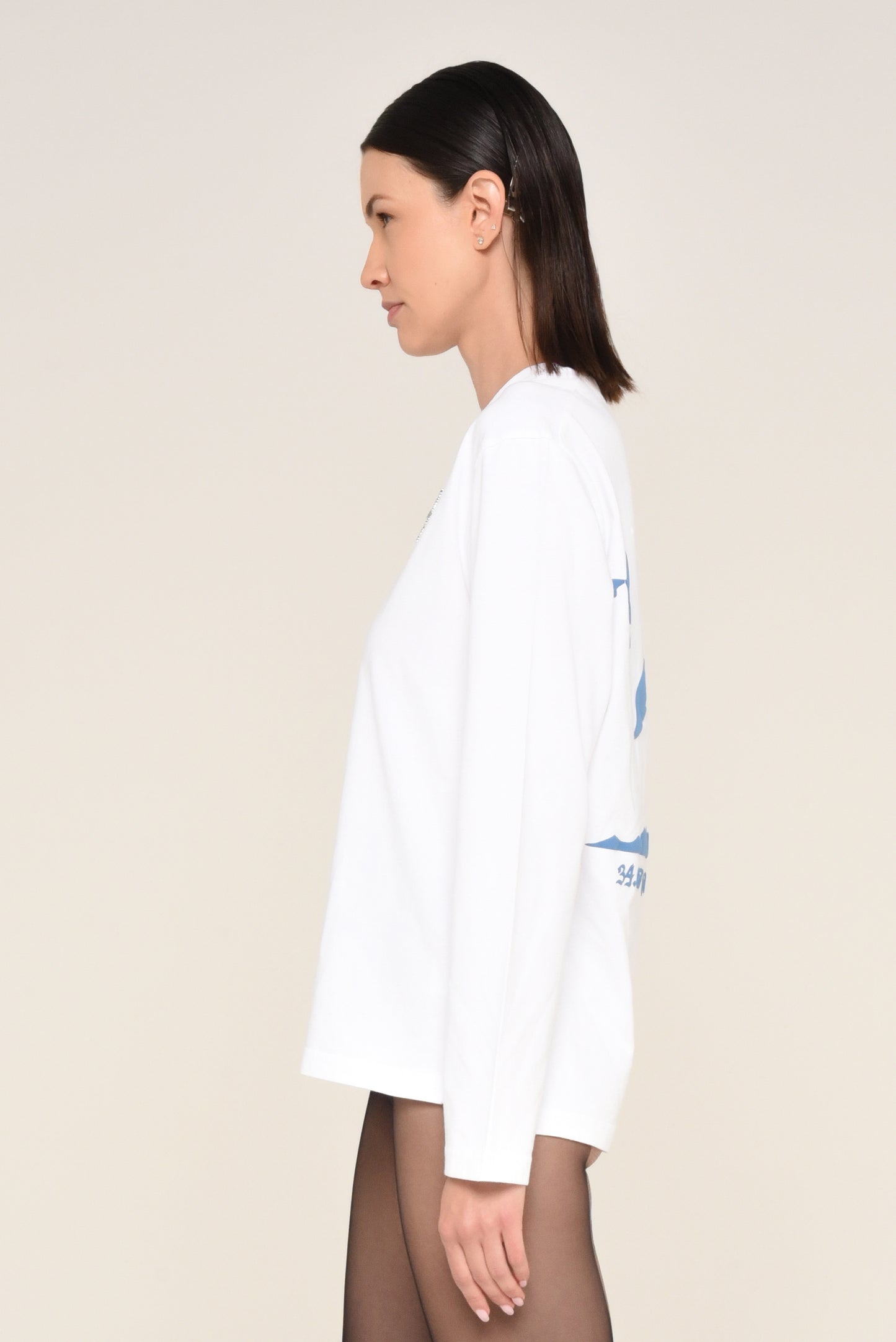 Side view of woman wearing a white long-sleeve shirt with cross detail and red text